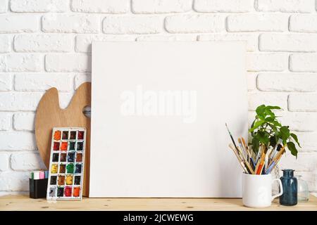 Cadre photo comme chevalet avec les outils de l'artiste sur une table en bois contre un mur en brique blanche Banque D'Images