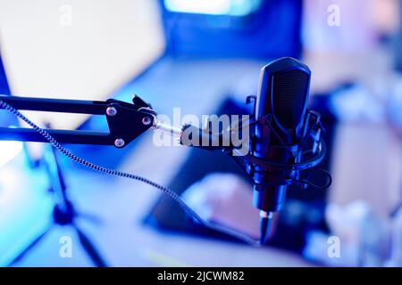 Gros plan du microphone professionnel sur le stand dans la configuration de diffusion de jeux vidéo éclairée par une lumière néon bleue, espace de copie Banque D'Images