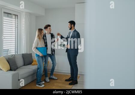 Heureux jeune couple achetant leur nouvelle maison et de recevoir des clés de l'agent immobilier Banque D'Images