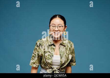 Portrait minimal d'une jeune fille asiatique portant des lunettes et souriant sur fond bleu, espace de copie Banque D'Images