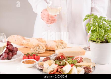 Femme tenant un verre de vin et servant des antipasti italiens traditionnels. Assiette de charcuterie avec différents types de saucisses - salami, bresaola, prostcu Banque D'Images