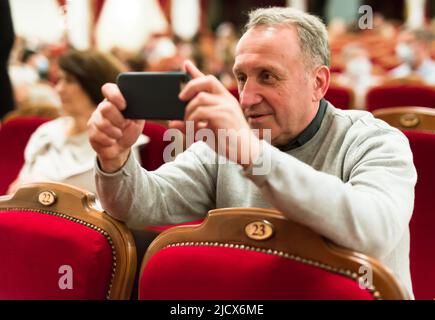 l'homme prend une photo de la performance avec son téléphone dans la salle de théâtre Banque D'Images