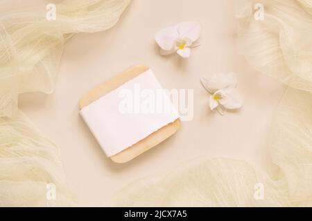 Bar à savon Hanmade près de fleurs d'orchidées blanches et tulle sur jaune clair, vue de dessus, maquette. Produit de beauté pour les soins de la peau. Cosmétiques naturels exotiques, pastel mini Banque D'Images