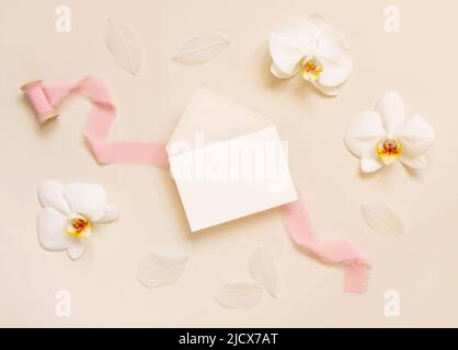 Enveloppe de mariage près de fleurs d'orchidées blanches et rubans de soie sur jaune clair vue de dessus, maquette. Scène tropicale avec carte horizontale vierge à plat Banque D'Images