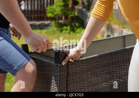 Un couple méconnaissable se déplace dans une nouvelle maison, assemble des meubles de canapé pour la terrasse, travaillant ensemble Banque D'Images