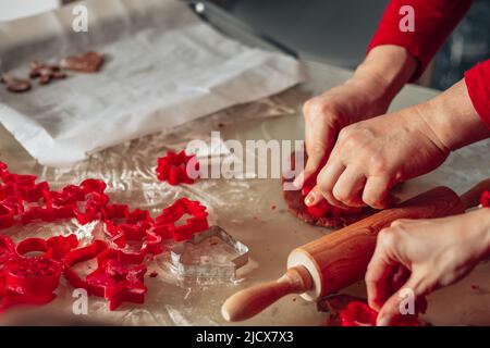 Gros plan des mains. L'homme et la femme ont coupé des biscuits de pâte. Pâtisseries de Noël, cuisine confortable, personnes méconnaissables. Couleur rouge. Saint-Sylvestre. Banque D'Images