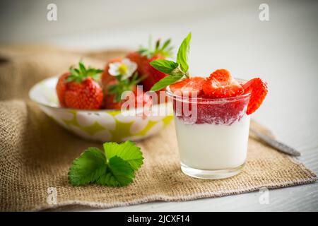 yaourt maison sucré avec confiture de fraises et fraises fraîches dans une tasse de verre, sur une table en bois. Banque D'Images