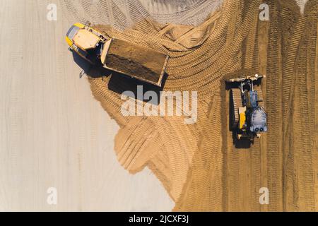 Vue extérieure aérienne d'un camion-benne chargé d'une pile de sable et d'un bulldozer déplaçant le sable faisant des traces dans le sable. Photo de haute qualité Banque D'Images