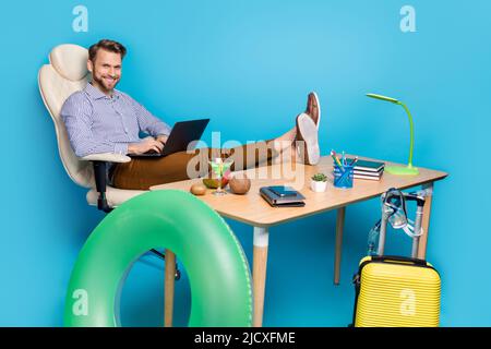 Portrait complet de l'homme joyeux et réussi fauteuil assis utiliser un netbook sans fil isolé sur fond bleu Banque D'Images