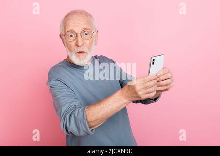 Photo de impressionné funky Guy retraité habillé gris pull-over verres écriture dispositif moderne isolé couleur rose fond Banque D'Images