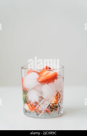 verre à l'eau tonique glacée avec des fraises hachées sur la surface blanche isolée sur le gris Banque D'Images