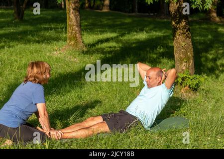 Homme faisant des croquises avec l'aide de sa femme pour être en forme et en bonne santé sorarrondie par la nature Banque D'Images