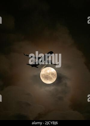Avion volant sur le chemin de la pleine lune la nuit Banque D'Images
