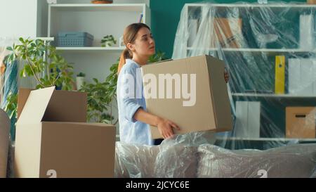 Une femme ressent une douleur soudaine au dos lorsqu'elle tente de soulever une boîte à carton. Femme utilisant un massage de la main sur sa douleur de dos. Une femme éprouve une gêne dans un résultat Banque D'Images