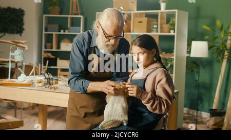 Un grand-père de Caring enseigne à sa petite-fille adolescente à coudre dans l'atelier Banque D'Images