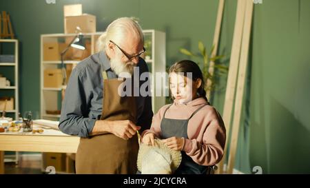 Un grand-père de Caring enseigne à sa petite-fille adolescente à coudre dans l'atelier Banque D'Images