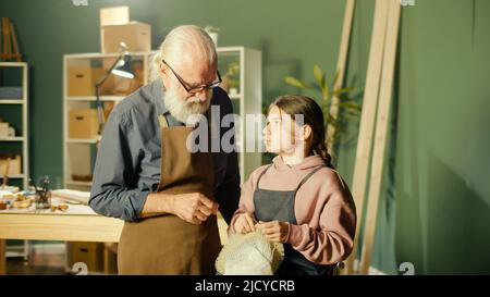 Un grand-père de Caring enseigne à sa petite-fille adolescente à coudre dans l'atelier Banque D'Images