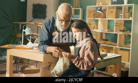 Un grand-père de Caring enseigne à sa petite-fille adolescente à coudre dans l'atelier Banque D'Images