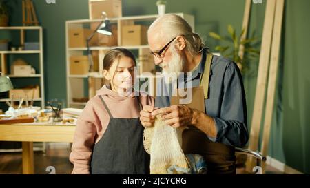 Un grand-père de Caring enseigne à sa petite-fille adolescente à coudre dans l'atelier Banque D'Images