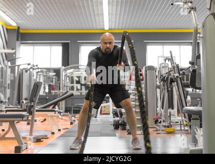 Photo d'un homme d'âge moyen ayant un dur entraînement avec des cordes dans une salle de gym. Sport dur et concept de motivation. Banque D'Images