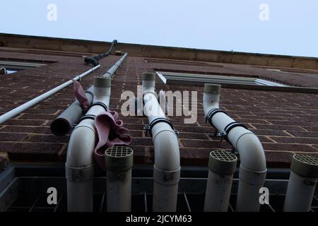 en regardant trois tuyaux en plastique sur le côté de un bâtiment avec des évents et des chiffons jetés Banque D'Images
