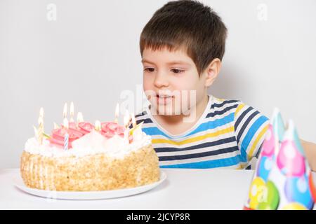 Un garçon célèbre son anniversaire assis à une table sur fond blanc avec un gâteau Banque D'Images