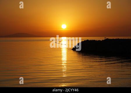 Une heure d'or pittoresque en bord de mer pendant un coucher de soleil aux couleurs orange vives avec une silhouette noire contrastée de jetée en pierre Banque D'Images