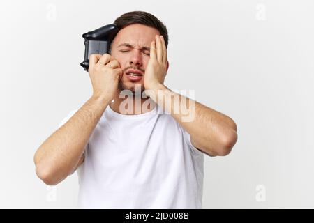 Fatigué frustré triste tannée beau homme dans le t-shirt de base perdre session de jeu face tactile avec manette de jeu posant isolé sur le studio blanc Banque D'Images