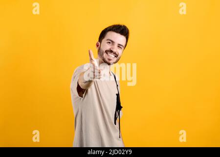 Joyeux homme décontracté portant un t-shirt posé isolé sur fond jaune s'étendant de la main à l'appareil photo, offrant la poignée de main. Accueil faire preuve de solidarité Banque D'Images
