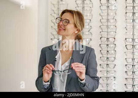 Femme d'affaires choisit un cadre de spectacle dans un magasin d'opticien Banque D'Images