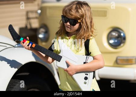 Portrait d'un enfant drôle avec des lunettes pratiquant une chanson pendant une leçon de guitare dans la rue. Concept de musique, école de musique pour enfants. Concert de rock. Enfant Banque D'Images