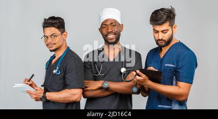 une équipe médicale attrayante debout sur fond gris clair. Infirmière afro-américaine et deux médecins indiens Banque D'Images