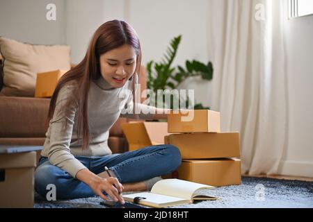 Jeune femme asiatique attrayante entrepreneur de PME emballage son colis dans la salle de séjour, préparant les commandes d'expédition. Banque D'Images