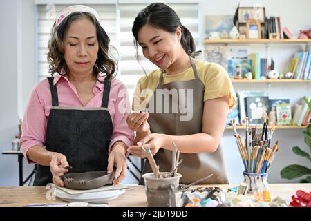 Attrayant charmant jeune artisan asiatique en céramique enseignant et l'entraînement de son élève de sexe féminin à faire un bol d'argile dans l'atelier. Banque D'Images