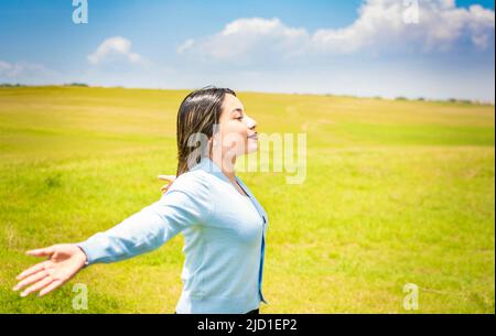 Femme heureuse respirant de l'air frais dans le champ et se propageant les bras, jeune femme souriant et se répandant les mains dans le champ vert, concept de femme Banque D'Images