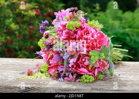 Bouquet coloré de fleurs dans les tons rouge, rose et violet avec des pivoines et des columbines, allongé sur des planches de bois abîmées dans le jardin Banque D'Images