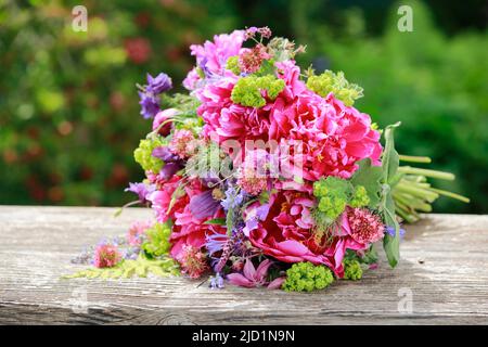 Bouquet coloré de fleurs dans les tons rouge, rose et violet avec des pivoines et des columbines, allongé sur des planches de bois abîmées dans le jardin Banque D'Images