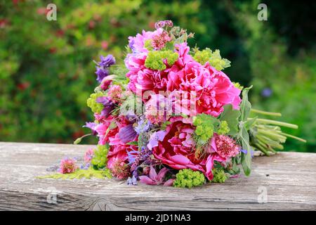 Bouquet coloré de fleurs dans les tons rouge, rose et violet avec des pivoines et des columbines, allongé sur des planches de bois abîmées dans le jardin Banque D'Images