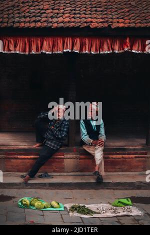 Deux vieux vendeurs de légumes à Bhaktapur, une ville de la vallée de Kathmadu au Népal. Les hommes sont assis dans une structure publique typique. Banque D'Images