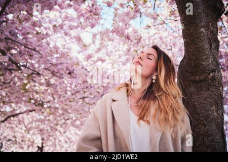 Jeune femme debout sous la fleur de cerisier Banque D'Images