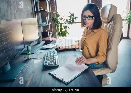 Portrait d'une fille habile, intelligente et attirante, une femme leader, compétente, qui lit des documents en développement sur un poste de travail à l'intérieur Banque D'Images