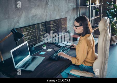 Profil vue latérale portrait d'une jeune fille attirante et spécialisée développeur Web utilisant un ordinateur portable sur le poste de travail à l'intérieur Banque D'Images