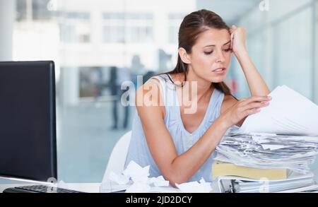 Enfoui sous la paperasserie. Photo d'une jeune femme d'affaires stressée qui passe par une pile de documents administratifs. Banque D'Images