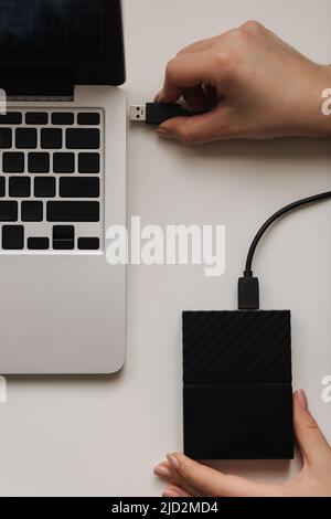 Disque dur portable femelle connecté à la main à l'ordinateur portable pour le transfert de données. Fichiers de sauvegarde. Copier le fichier. Vue de dessus. SSD noir Banque D'Images