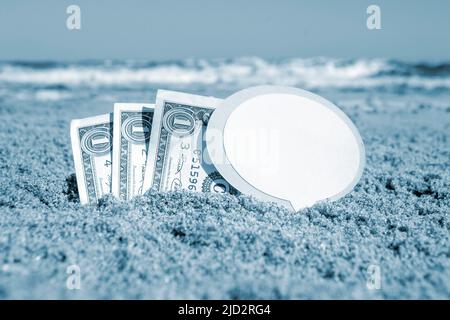 Billets de papier un dollar, un petit bâton propre papier vide bulle de parole enfouie dans le sable plage arrière-plan mer gros plan dans la journée ensoleillée d'été. Concept argent voyage tourisme vacances. Bleu blanc Banque D'Images