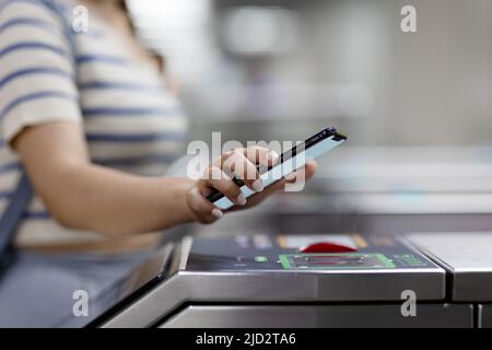 Prise de vue rognée d'une jeune femme asiatique qui scanne le code QR, s'enregistrer à la station de métro, ce qui permet un paiement sans contact rapide et facile du billet de métro via s.