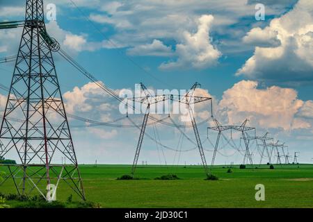 Rangée de pylônes de soutien de ligne de puissance sur le champ vert cultivé avec ciel nuageux. Équipement de transition d'énergie. Banque D'Images