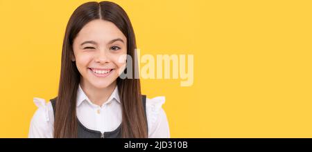 Bonne fille d'âge scolaire fille avec visage souriant donner un fond jaune de clin d'œil, de la givelle. Visage d'enfant, affiche horizontale, portrait isolé de jeune fille Banque D'Images