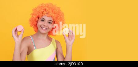 bonne adolescente en maillot de bain portant perruque tenir macaron français sur fond jaune. Adolescent avec bonbons, affiche en-tête de bannière, espace de copie. Banque D'Images