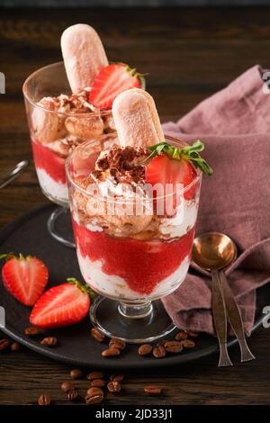 Tiramisu fraise. Dessert italien traditionnel tiramisu en verre avec feuilles de fraise et de menthe fraîches sur fond de table sombre en bois. Station santé Copy Banque D'Images